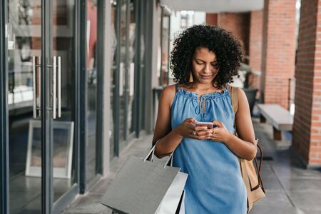 Smiling woman using her cellphone while out shoppingの写真素材