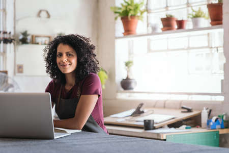 Smiling woman working on a laptop in her framing shopの写真素材