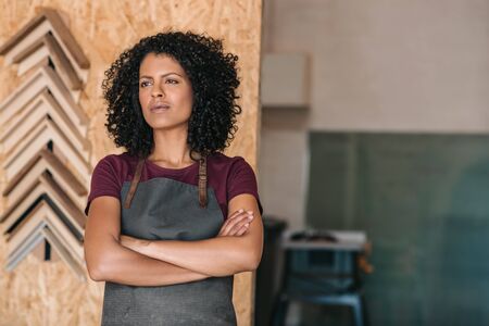 Confident young woman standing in her picture framing workshopの写真素材