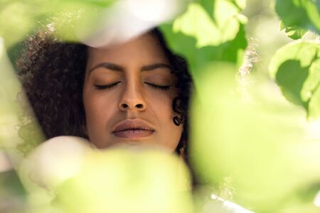 Young woman with her eyes closed framed by green leavesの写真素材