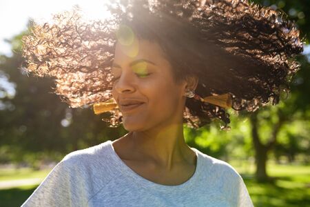 Smiling woman twirling her curly hair outside in a parkの写真素材