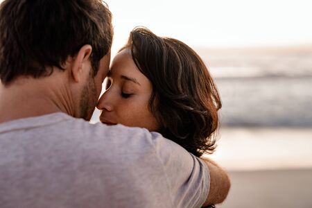 Loving woman standing in her husbands arms on a beachの写真素材