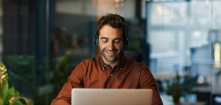 Smiling businessman talking on a headset and using a laptopの写真素材