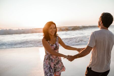 Laughing young couple having fun at the beach at sunsetの写真素材