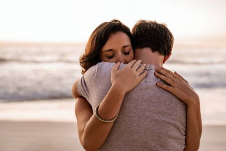 Loving woman hugging her husband on a beach at duskの写真素材