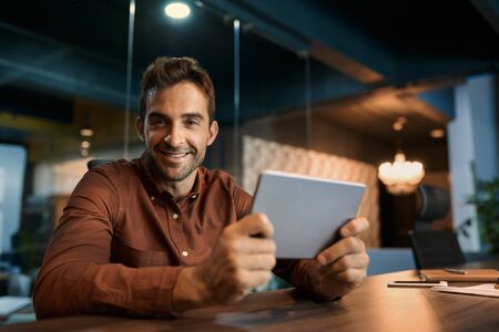 Smiling businessman working on a tablet at his office deskの写真素材
