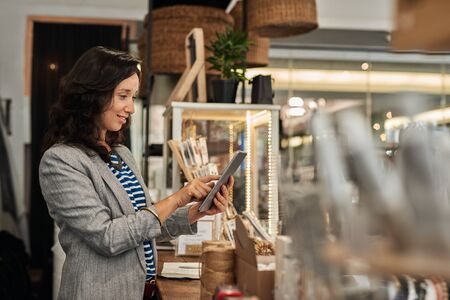 Smiling young Asian woman using a tablet in her storeの写真素材