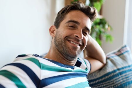 Smiling young man relaxing on his living room sofaの写真素材