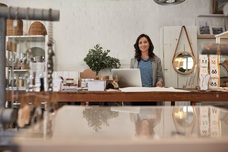 Smiling Asian woman working behind a counter in her shopの写真素材