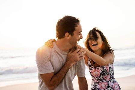 Laughing couple having fun together on a beach at sunsetの写真素材