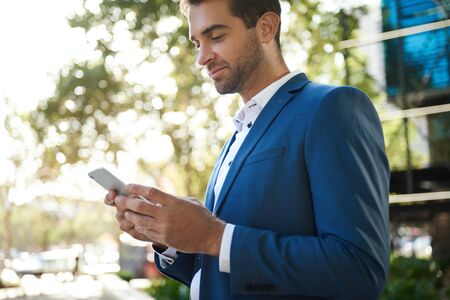 Young businessman standing outside sending a text on his cellphoneの写真素材