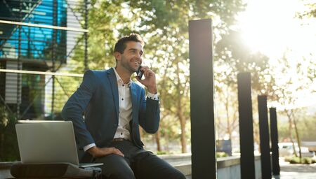 Smiling businessman talking on a cellphone outside his office buildingの写真素材