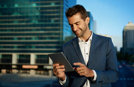 Smiling businessman working on a tablet on an office terraceの写真素材