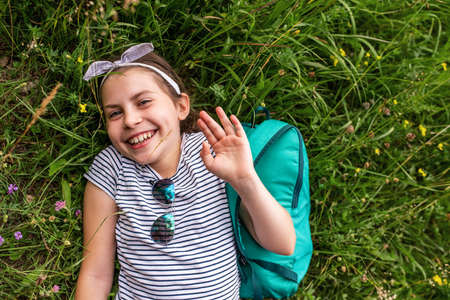 Cute little girl waving hi while lying on some grassの写真素材