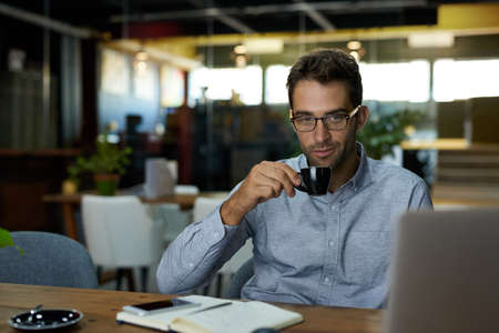 Young businessman drinking coffee at his office deskの写真素材