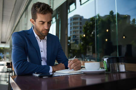Businessman writing in a notebook at a sidewalk cafe tableの写真素材