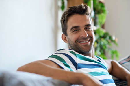 Smiling young man relaxing at home on his sofaの写真素材
