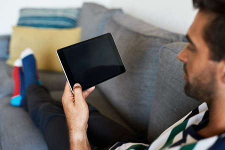 Man relaxing on his sofa and using a digital tabletの写真素材