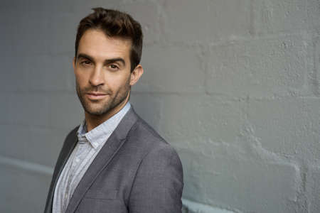 Confident businessman leaning against a brick wall in an officeの写真素材