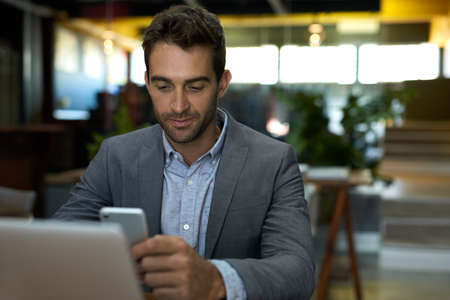 Businessman checking his cellphone while working alone in an office