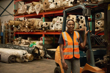 Young African female forklift operator standing in a warehouseの写真素材
