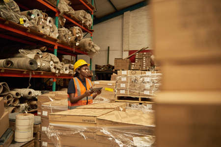 African female warehouse worker checking boxes using a digital tabletの写真素材