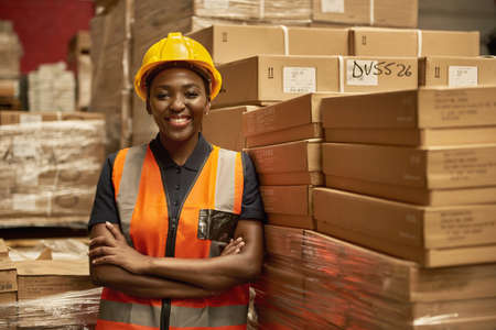 Smiling African female warehouse worker leaning against some boxesの写真素材