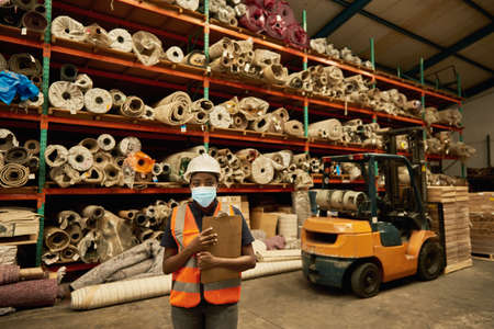 African worker standing in a warehouse wearing a face maskの写真素材