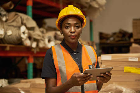 Young African female warehouse worker doing inventory with a tabletの写真素材