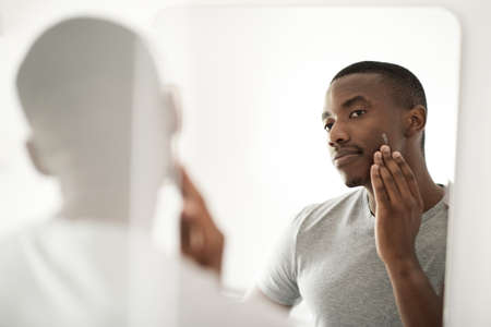 African man applying lotion on his face in his bathroom mirrorの写真素材