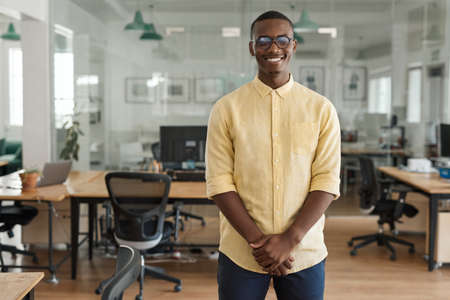 Smiling young African businessman standing in a modern officeの写真素材