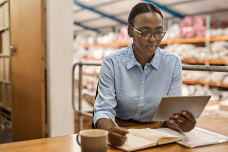 Young African woman working on a tablet at her warehouse deskの写真素材