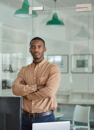 Confident African businessman standing with his arms crossed in an officeの写真素材