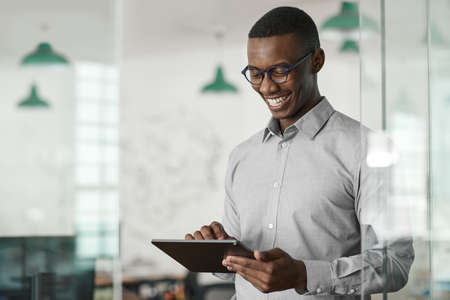 Smiling young African businessman using a digital tablet at workの写真素材