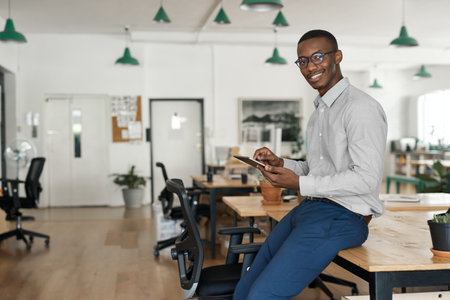 African businessman smiling while using a tablet at his office deskの写真素材