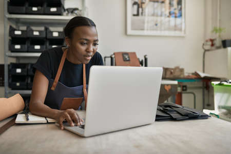 African female leather worker using a laptop at a workbenchの写真素材