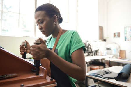 Young African female leather worker using a cutting machineの写真素材