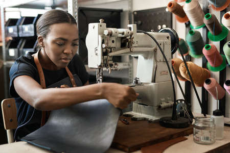 Young African female artisan sewing leather in her workshopの写真素材