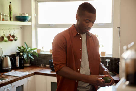 Young African man cutting an avocado at his kitchen counterの写真素材