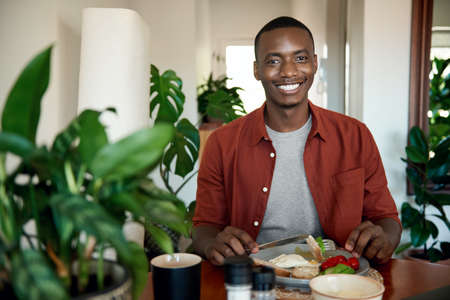 Smiling young African man eating breakfast at his dining table