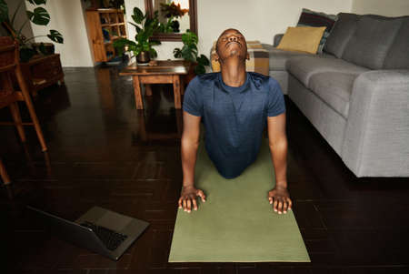 Young African man doing the cobra pose during yoga at homeの写真素材