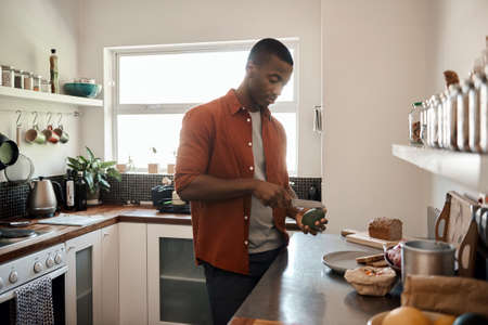 Young African man cutting an avocado in his kitchenの写真素材