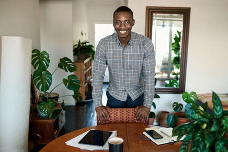 Smiling African businessman leaning on a table while working from homeの写真素材