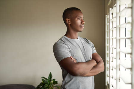 Young African man looking out through a window at homeの写真素材