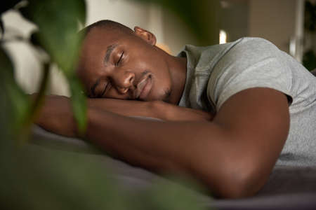 Young African man sleeping in his bed at homeの写真素材