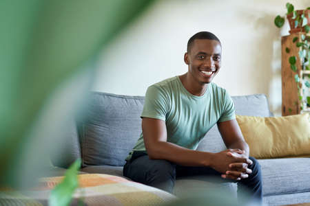 Smiling young African man sitting on his sofa at homeの写真素材