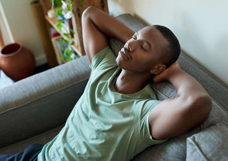 Young African man lying back on his living room sofaの写真素材
