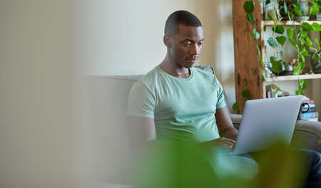 Young African man using a laptop while sitting on his sofaの写真素材