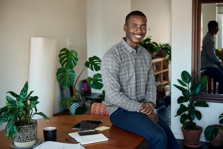 Smiling African businessman sitting on a table while working from homeの写真素材