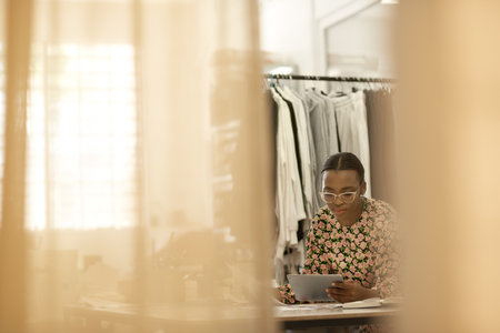 African female clothes designer working on a tablet at studio tableの写真素材